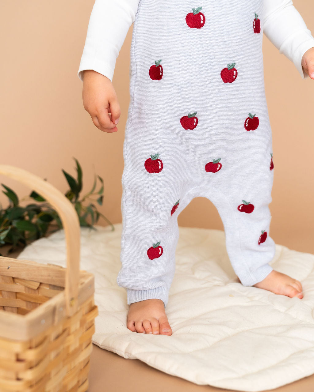 Baby wearing Viverano Organics organic cotton baby overall set with red apple embroidery standing on a quilted mat