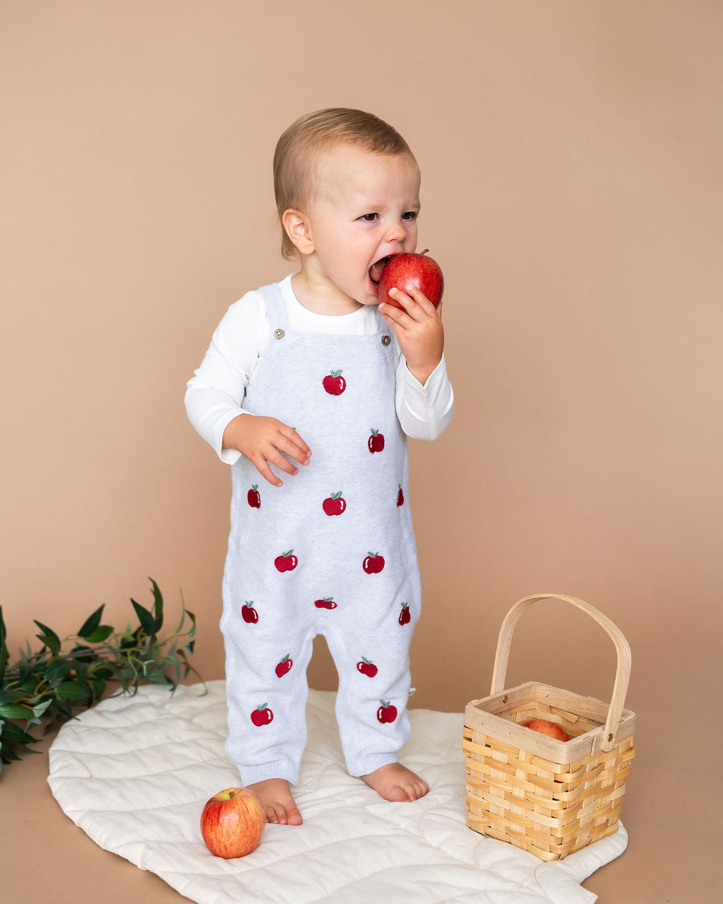 Baby wearing Viverano Organics organic cotton baby overall set with apple embroidery eating a red apple