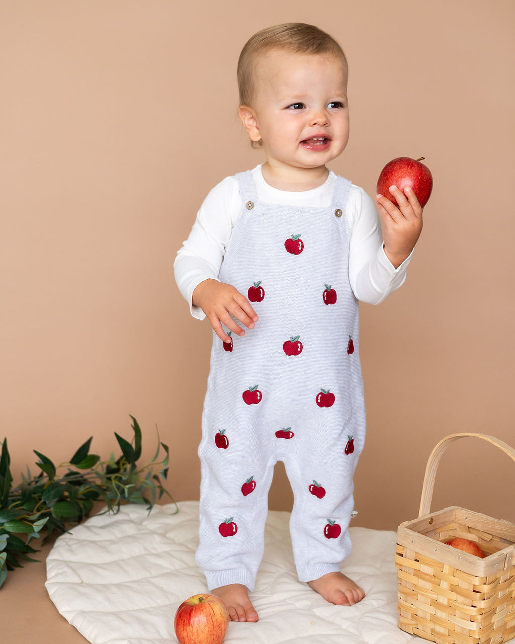 Viverano Organics organic cotton baby overall set with red apple embroidery worn by a toddler holding a red apple